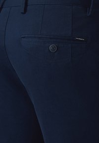 Granatowe, fakturowane spodnie z tylną kieszenią, z zapięciem na guzik oraz małą metką marki blisko szwu.