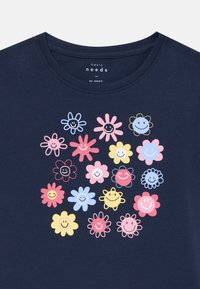 Mørkeblå t-skjorte med rund hals, som har et fargerikt trykk av smilende blomster i rosa, gult og blått. Myk, bomullsstoff.
