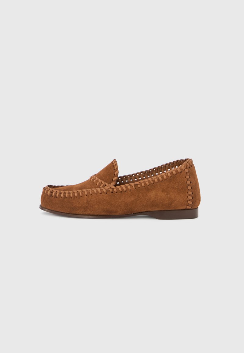Mocassins en daim marron avec un bout arrondi, des coutures le long des bords, et une semelle à profil bas. Texture douce avec des accents de design minimalistes.