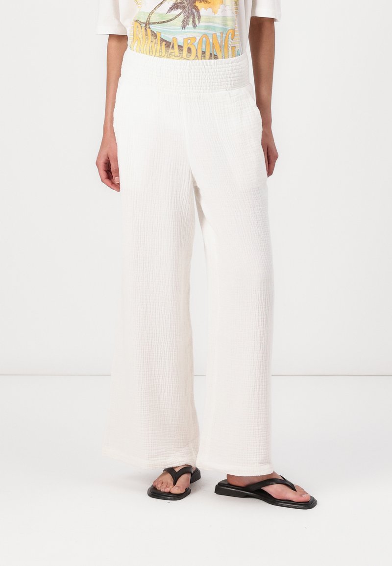 Pantaloni bianchi a gamba larga realizzati in tessuto testurizzato con una vita smock, caratterizzati da una vestibilità ampia e un orlo che sfiora leggermente il pavimento.