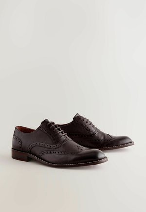 Chaussures en cuir de couleur brun foncé avec un design à bout fleuri, des accents texturés, des détails perforés et une couture contrastante de couleur claire le long de la semelle.