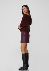 Suéter de punto burdeos estilo off-shoulder, combinado con una falda de cuero morada ajustada y botas negras hasta la rodilla de textura suave.