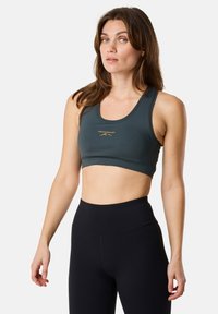 Mörkgrön sportbh med rund halsringning och en åtsittande design. Har guldtext framtill. Kombineras med högmidjade svarta leggings.