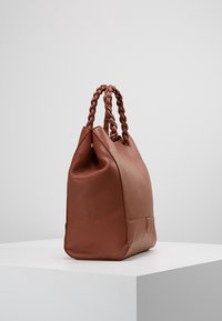 Bruine leren handtas met een gestructureerde afwerking, ronde vorm en gevlochten handvatten. De basis is plat en breed, wat zorgt voor stabiliteit.