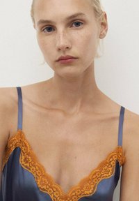 Satin camisole in deep blue with intricate orange lace trim along the neckline and straps, showcasing smooth texture and elegant design.