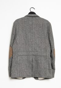 Grå herringbone-blazer med bruna armbågsrestauranger, enkelknäppt design och en mjuk textur. Hänger på en svart krok.