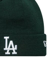 Bonnet en tricot vert avec un revers. Présente un logo "LA" brodé en blanc sur le devant et une petite marque blanche sur le côté. Texture douce.