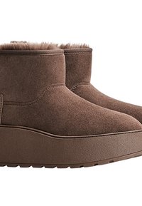Stivaletti in suede marrone con suole spesse e piattaforma e foderatura in pelliccia visibile sui bordi superiori, su uno sfondo bianco.