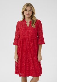Red lace dress with a v-neckline and three-quarter sleeves. Features floral patterns and a flared silhouette, made from lightweight fabric.