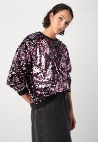 Sudadera adornada con lentejuelas en tonos negros y rosas, con un cuello redondo y puños acanalados. Textura suave y brillante con un corte oversize.
