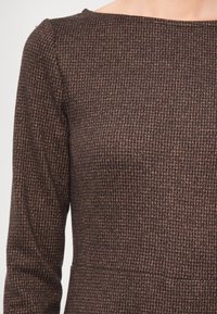 Brun teksturert kjole med et subtilt geometrisk mønster, lange ermer og rund hals, laget av et mykt, vevd stoff.