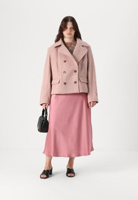 Heledad roosa topeltklõpsudega jakk, millel on tekstureeritud kangas, suured kraed ja pruunid nupud, kantud roosa satiinist midi kleidi ning mustade aksessuaaridega.