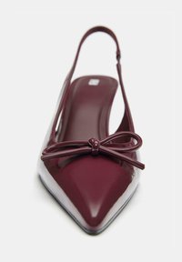 Burgundska slingback čevlja s koničastim nosom, ki ima sijajno površino, občutljiv detajl s pentljo na sprednji strani in prozoren visok peto.