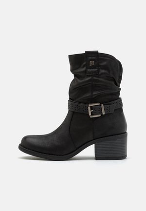 Black ankle boots with a slightly slouched top, decorative buckle, and cut-out pattern on the strap. Medium block heel and faux leather material.