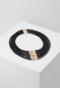 Collar negro de múltiples hebras que presenta cuerdas suaves y flexibles con acentos en tono dorado. Cada hebra está agrupada cerca del cierre, creando un efecto de capas.