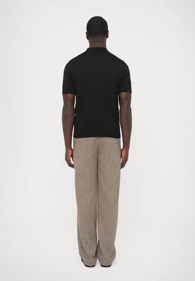 Polo preta de manga curta com gola clássica, combinada com calças largas castanhas em tecido texturado, vista de costas.