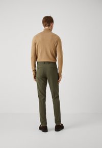 Brown knitted sweater, fitted olive green trousers with back pockets, and dark brown shoes, viewed from the back. Solid colors, smooth texture.