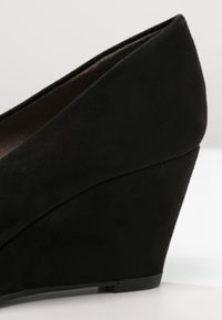 Black suede wedge shoe with a smooth texture, featuring a tapered shape and a low platform. The heel is solid with a matte finish.