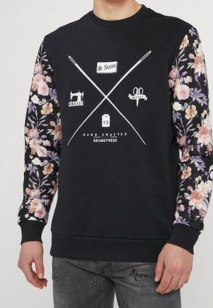 Černá mikina s květinovým vzorem na rukávech, s bílým textem a grafikou související s šitím. Žebrované manžety a výstřih.