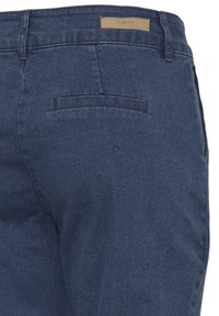 Sötétkék farmernadrág sima textúrával, hátsó zsebbel és a derékrészen található márkás, barna címkével.