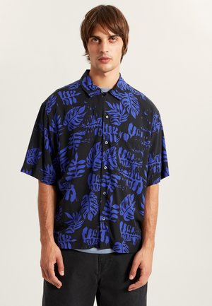 Koszula z krótkim rękawem w czarnym kolorze z intensywnym niebieskim nadrukiem liści, zapinana z przodu na guziki, o luźnym kroju.