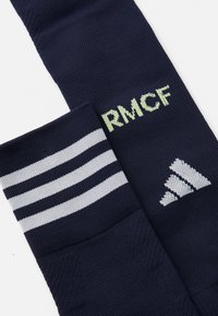 Marine sportsokker med lysegrå striper, "RM CF"-logo i lysegrønn, og Adidas-logo i hvitt. Laget av teksturert stoff.