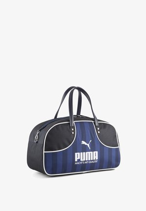 Czarna i niebieska torba sportowa Puma w paski, z białym logo i napisem, uchwyty do noszenia oraz zamknięcie na zamek błyskawiczny na górze.