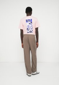 Ρόδινο κοντομάνικο μπλουζάκι με μπλε και λευκό γραφικό σχέδιο στην πλάτη. Καφέ παντελόνι με άσπρες λωρίδες στο πλάι και άνετα υποδήματα.