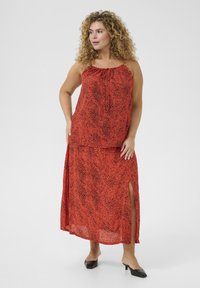 Robe deux pièces à motifs rouges avec une silhouette fluide. Le haut possède des bretelles ajustables et un détail à nouer, tandis que la jupe présente des fentes sur les côtés.