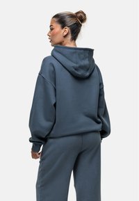 Felpa con cappuccio di colore grigio scuro, caratterizzata da una vestibilità comoda, materiale morbido e polsini a costine. Abbinata a pantaloni della tuta coordinati.