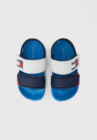 Białe i granatowe klapki na spodzie w kolorze niebieskim, z regulowanymi paskami i logo w akcentach czerwonym i niebieskim. Podeszwa o fakturze.