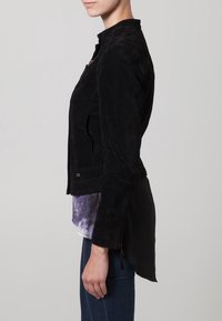 Svart mockajacka med ståkrage, sidodragkedja och längre bakre fåll. Bärs över en flerfärgad topp och matchas med tajta jeans.