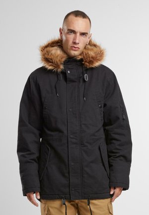 Parka negra con capucha de piel sintética desmontable, que cuenta con cierres de cremallera y automáticos, puños elásticos y múltiples bolsillos para mayor funcionalidad.