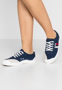 Marineblå kanvas sneakers med hvide snøreb�ånd, grå og hvide detaljer, rund tå og struktureret gummisål, med ventilationshuller.