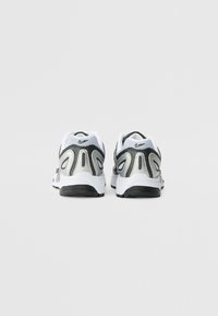Balti ir pilki sportiniai batai su tinkliniu viršumi, apvaliu kulnu ir juoda trakcionine pada; turi „Nike“ logotipą ir metalinius akcentus.