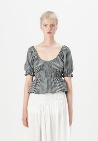 Top peplum a quadretti bianchi e neri con maniche a palloncino corte e scollatura profonda, abbinato a una gonna bianca con pieghe. Tessuto crisp e strutturato.