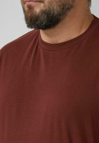 Bordowa koszulka z krótkim rękawem wykonana z miękkiej bawełny; posiada klasyczny okrągły dekolt i gładką teksturę bez widocznych wzorów czy akcentów.