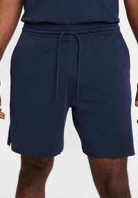 Pantalones cortos azul marino hechos de una tela suave, con una cinturilla elástica y cordón ajustable, y con cortes laterales para mayor comodidad de movimiento.