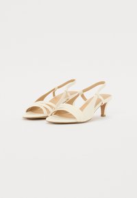 Helle Slingback-High Heels mit offener Zehenpartie, versehen mit einem überkreuzten Riemen-Design und einem schlichten Kegelabsatz. Glatte Textur, minimale Hardware.
