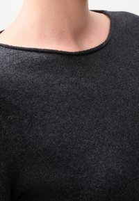 Gros plan sur le cou et le haut de la poitrine d'une personne portant un pull ras du cou gris foncé avec une texture fine et douce.