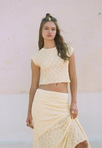 Ensemble en dentelle à deux pièces de couleur jaune pâle ; top court à manches courtes, jupe évasée avec détail drapé, le tout ornée de motifs complexes.