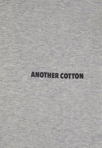 Tricou din bumbac gri cu textul "ANOTHER COTTON" imprimat cu litere negre îngroșate în centru. Textură netedă, design casual.