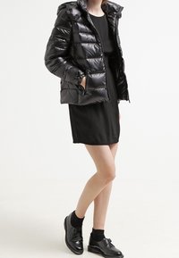 Black puffer jacket with a glossy finish, featuring a hood and zippered pockets, paired with a black dress and black shoes.