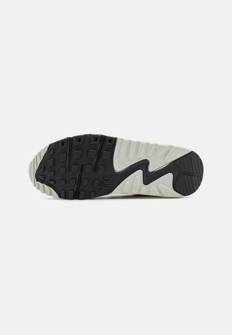Suela de zapatilla negra y blanco roto con una superficie texturizada, patrones de goma distintivos y un acento de logotipo visible cerca del talón.
