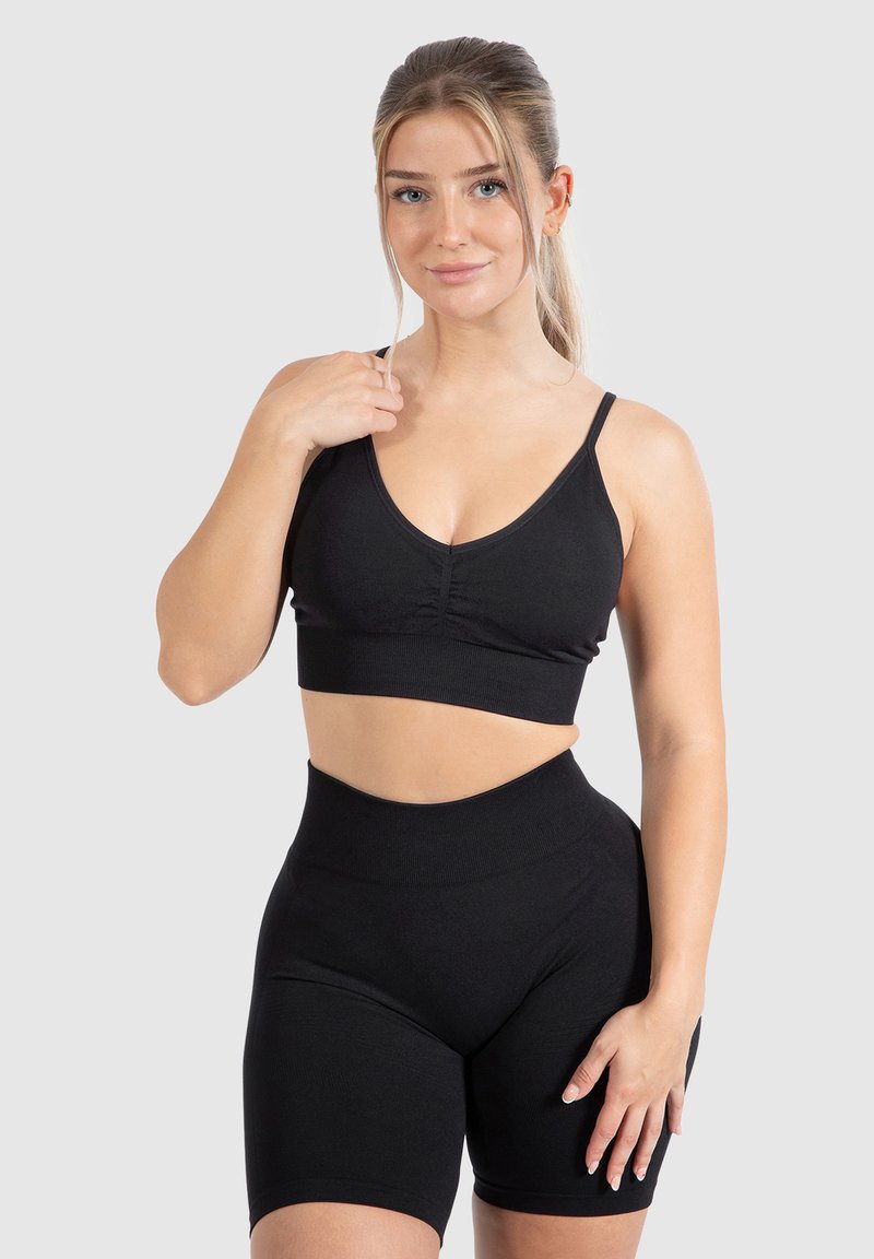 Zwarte sport BH met verstelbare dunne banden en een geplooid midden, gecombineerd met hoge zwarte fietsbroek in een soepele stof.