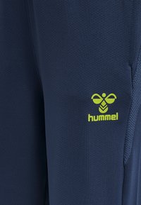 Marineblauwe sportbroeken met een gestructureerd oppervlak, voorzien van een limoengroene "hummel"-logo op de dij en een aansluitend ontwerp voor comfort.