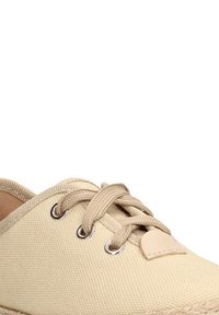 Zapatilla de lona beige con punta redonda, dos ojales y cordones beige. Presenta un acento de cuero marrón y una superficie de tela texturizada.