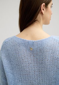 Jasnoniebieski sweter dzianinowy o luźnej, otwartej strukturze, z okrągłym dekoltem i małym, srebrnym logo z tyłu.