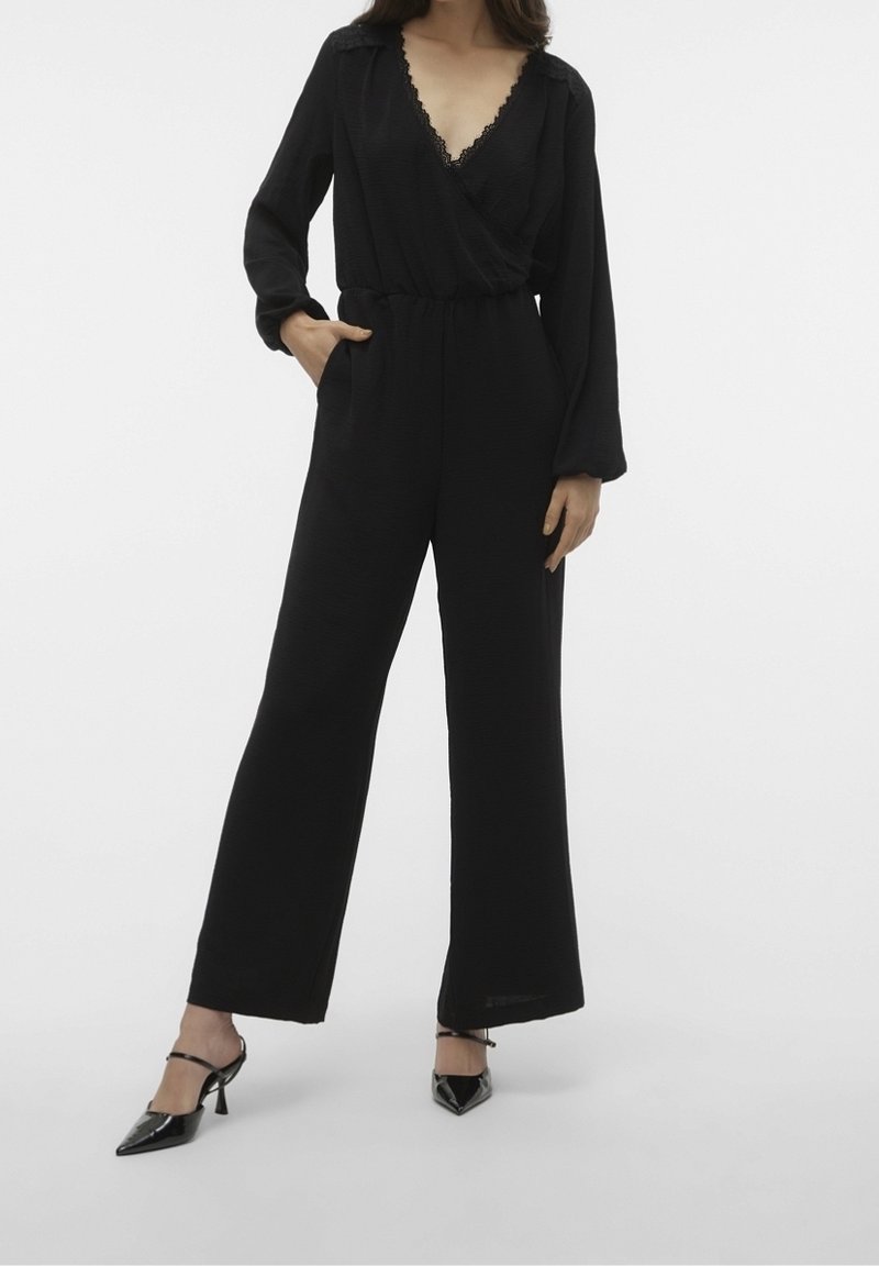 Black jumpsuit with long sleeves and a deep V-neck, featuring lace trim on the neckline, cinched waist, and wide leg cut.