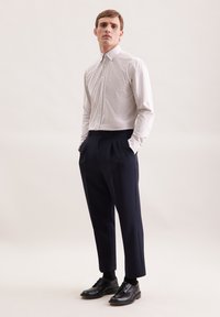 Camicia bianca a quadri con colletto a punta, abbinata a pantaloni navy scuri e scarpe in pelle nera, caratterizzate da pieghe.